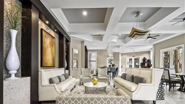 A modern living room with a sofa set, a patterned ottoman, and a dining area in the background.