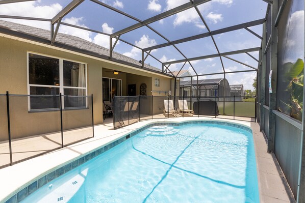 Une piscine entourée de parois en verre, un patio couvert et une vue sur une maison au loin.