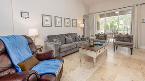 A living room with a brown leather sofa, a grey couch, and a wooden coffee table. There are framed pictures on the wall and a lamp on a side table. - Spacious 4-bedroom home in Kissimmee, perfect for family getaways! (Kissimmee)