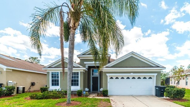 A single-story house with a front garage, a palm tree, and a well-maintained lawn. - Spacious 4-bedroom home in Kissimmee, perfect for family getaways! (Kissimmee)