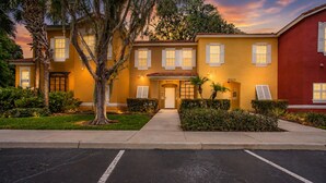 A yellow building with a red section, numbered 8405, and 8407, with a parking lot in front. - Charming 3-bedroom townhome in Kissimmee, perfect for family getaways! (Kissimmee)