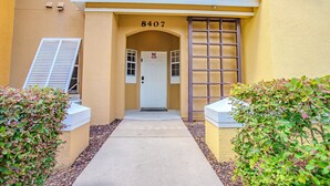 Een gebouw-ingang met het nummer '8407' boven de deur, een witte deur en een klein raam met luiken.