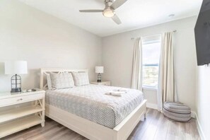 A bedroom with a bed, nightstands, a desk, a window with curtains, and a ceiling fan.
