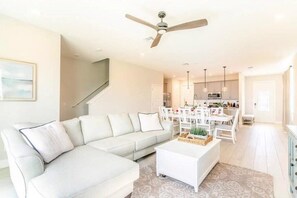 A modern living room with a white sofa, a coffee table, and a dining area with white chairs and a table.