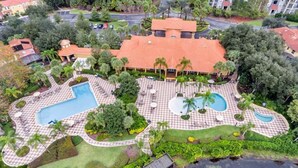 Een luchtbeeld van een resort met meerdere zwembaden, palmbomen en een groot gebouw met een rood dak.