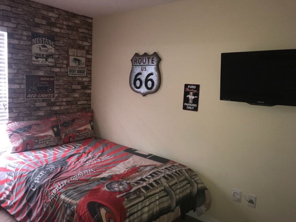 A bedroom with a bed, a brick wall, a Route 66 sign, a Ford parking sign, and a television.