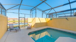 En inomhuspool med en glasvägg, två solstolar och utsikt över en vattenyta och byggnader i bakgrunden.