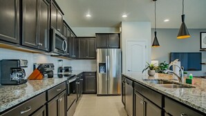 Una cocina moderna con armarios oscuros, electrodomésticos de acero inoxidable, encimeras de granito e iluminación colgante.