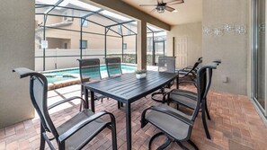 A patio with a table and chairs, a pool, and a glass enclosure.