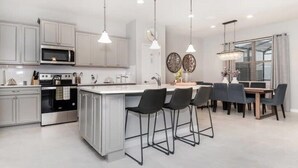 A modern kitchen with a central island, bar stools, and a dining area with a table and chairs. - Spacious 5-bedroom home in Kissimmee, perfect for family getaways! (Kissimmee)