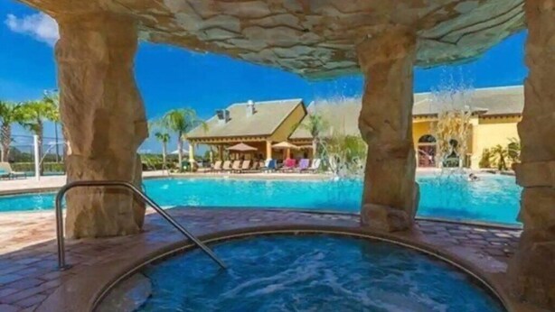A hot tub area with a pool and a building in the background. - Spacious 4BR Kissimmee Townhome with Private Pool, sleeps 12 in Paradise Palms. (Kissimmee)