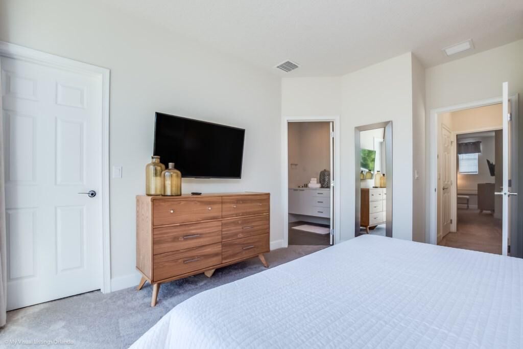 A bedroom with a large bed, a dresser, a flat-screen TV, and a walk-in closet.