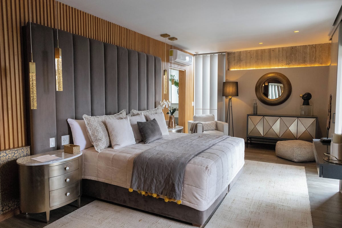 Une chambre à coucher moderne avec un grand lit, des tables de chevet, un miroir rond et un panneau décoratif mural.