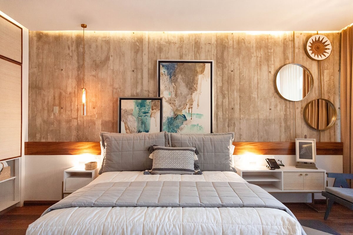 Une chambre moderne avec un grand lit, deux tables de chevet, une petite table et un miroir fixé au mur.