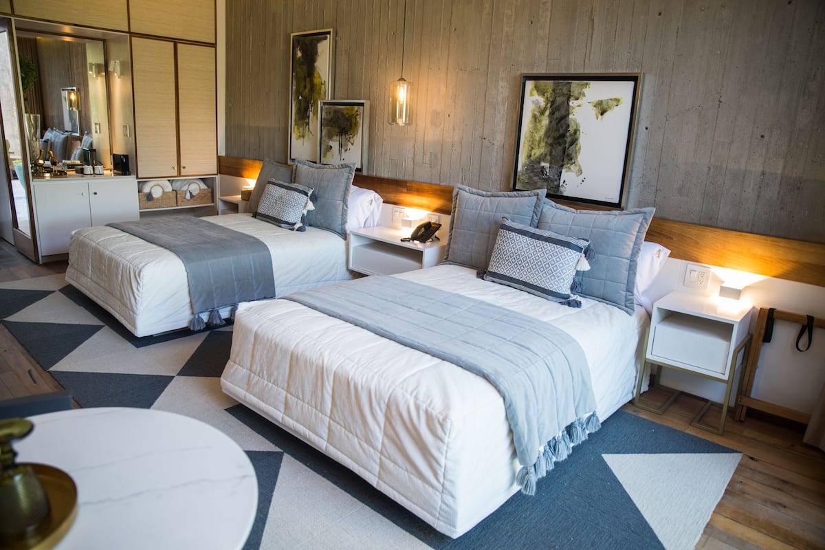 Une chambre d’hôtel moderne avec deux lits, un grand miroir, des tables de chevet avec des lampes et des œuvres d’art accrochées aux murs.