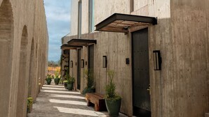 Un pati amb un camí pavimentat, un edifici amb una banca de fusta i plantes en testos.