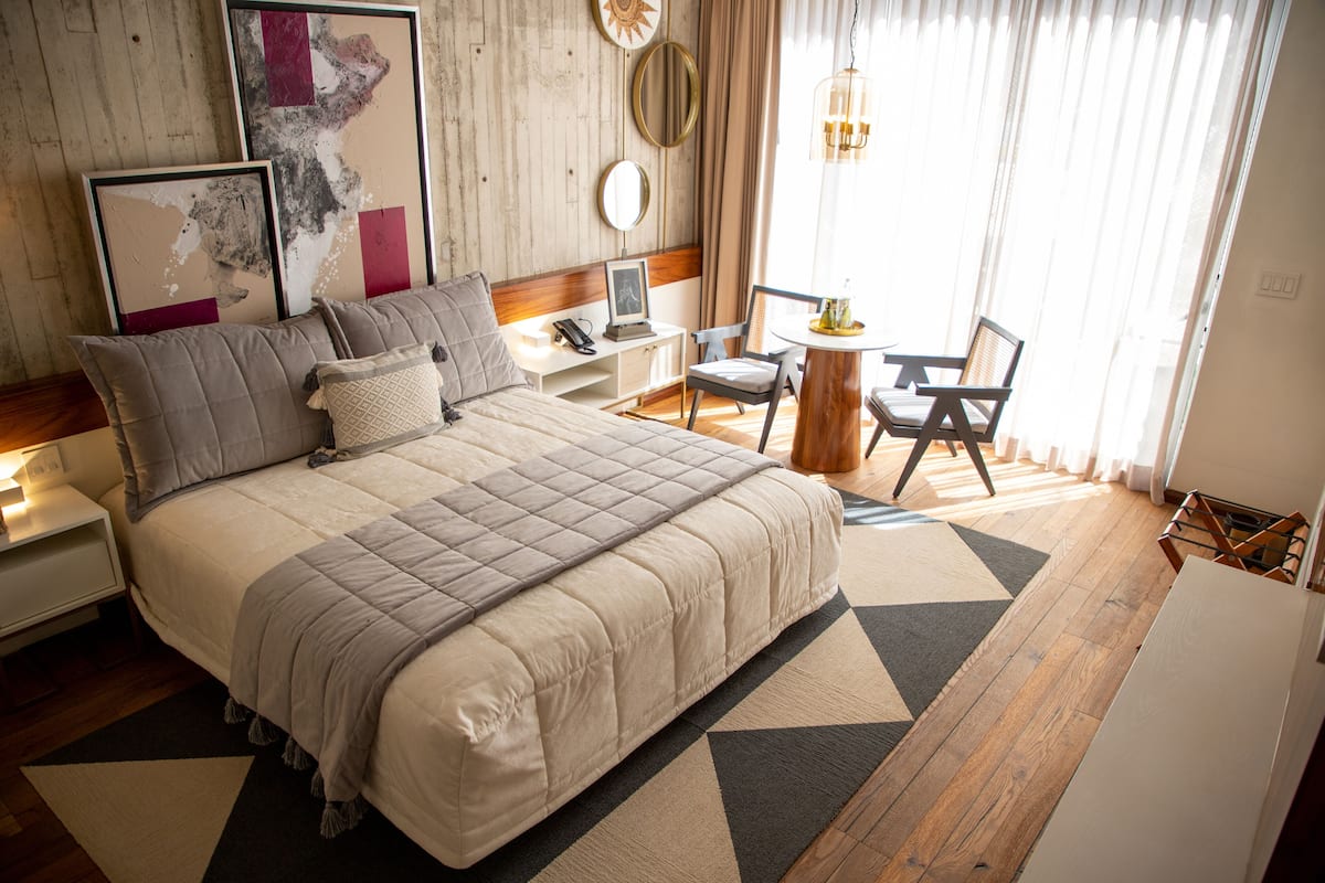 Une chambre bien rangée, avec un grand lit, des tables de chevet, une chaise et une petite table.