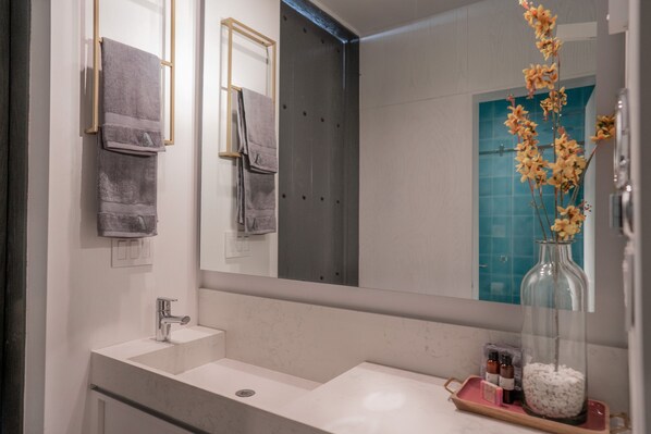 Un baño moderno con un espejo grande, un lavabo blanco y una jarrón de cristal con flores.