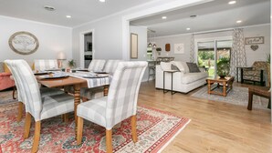 A spacious living room with a dining area, featuring a large window, a sofa, a coffee table, and a rug.