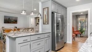 A modern kitchen with grey cabinets, a stainless steel refrigerator, and pendant lighting.