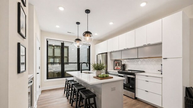 A modern kitchen with a central island, bar stools, stainless steel appliances, and pendant lighting. - Rooftop • King Beds • Near Light Rail & LoSo (Charlotte)