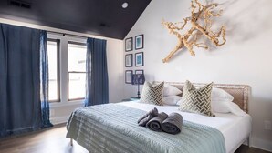 A bedroom with a large bed, a ceiling with a skylight, and a wall-mounted decor piece. - Rooftop • King Beds • Near Light Rail & LoSo (Charlotte)