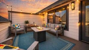 An outdoor patio with a fire pit, seating, string lights, and a view of the sunset. - Rooftop • King Beds • Near Light Rail & LoSo (Charlotte)