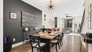A dining area with a long table, chairs, and a chandelier. There is a staircase leading to an upper level. - Rooftop • King Beds • Near Light Rail & LoSo (Charlotte)