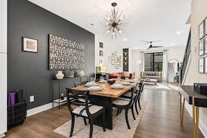 A dining area with a long table, chairs, and a chandelier. There is a staircase leading to an upper level. - Rooftop • King Beds • Near Light Rail & LoSo (Charlotte)