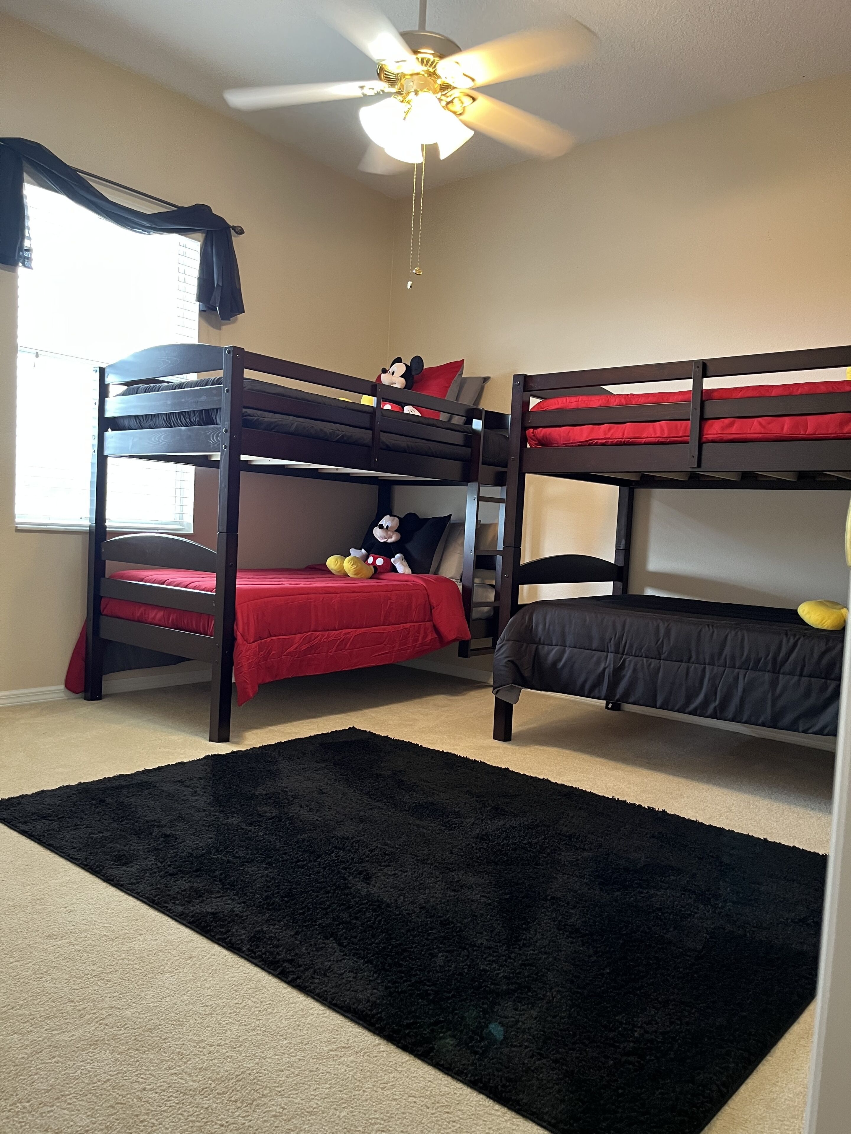 A room with two bunk beds, a ceiling fan, and a window with blinds.