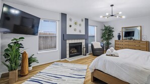 Une chambre moderne avec une cheminée, un grand lit, une télévision et un luminaire au plafond.
