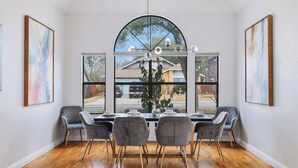 Un coin repas avec une grande fenêtre en arc de cercle, une table dressée pour quatre personnes et deux chaises grises aux pieds en bois.