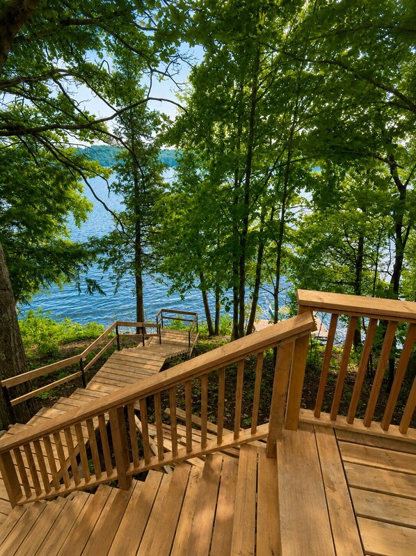 Une terrasse en bois dotée d’une rambarde, qui mène à une étendue d’eau bordée d’arbres.
