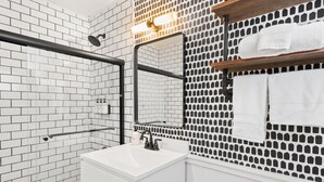 A modern bathroom with white subway tiles, a glass shower enclosure, a white sink, and a mirror with a black frame. - Standard Room w/ King Bed, Balcony, Fireplace, Mountain Views Room #13 (Lake Placid)