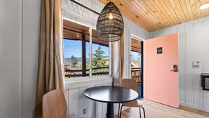 A room with a round table, two chairs, a hanging light fixture, a door with a number, and a window with curtains. - Standard Room w/ King Bed, Balcony, Fireplace, Mountain Views Room #13 (Lake Placid)