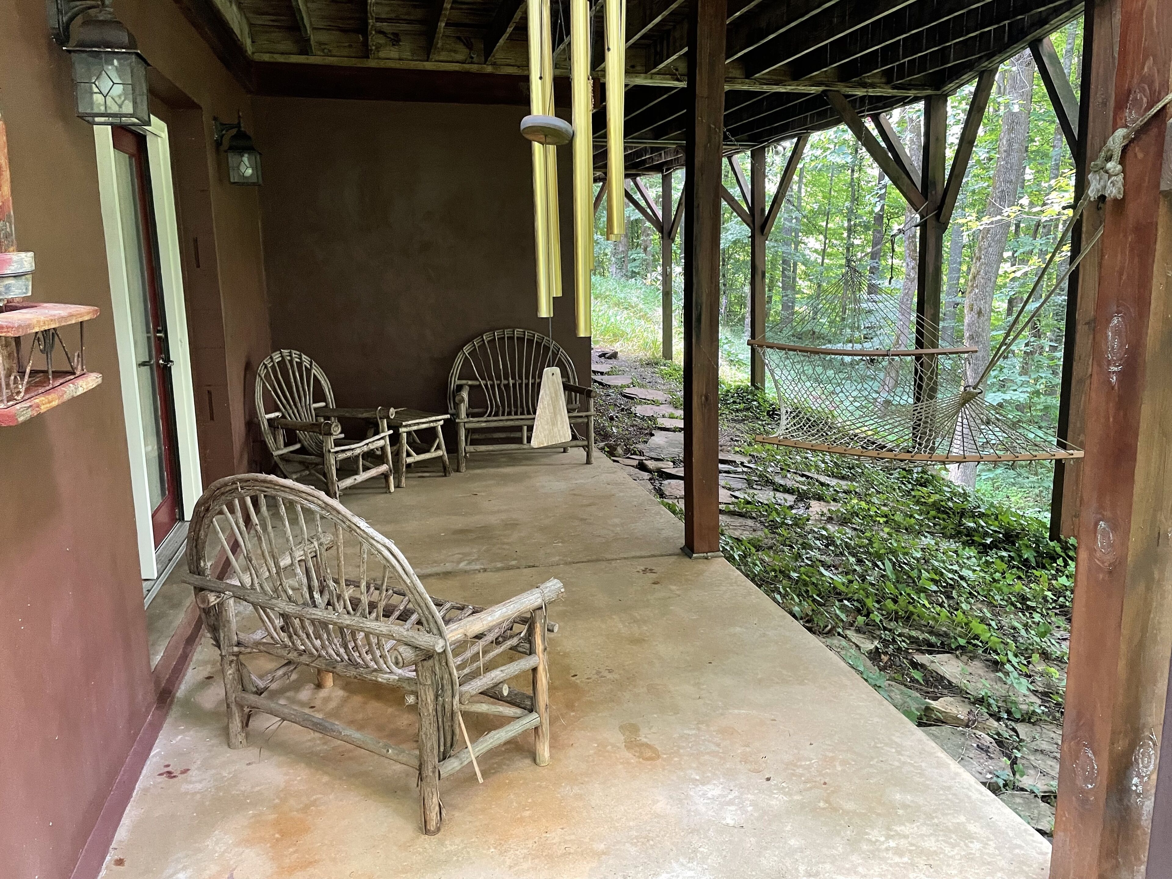 A covered outdoor seating area with rustic wooden furniture and a view of a forested area.