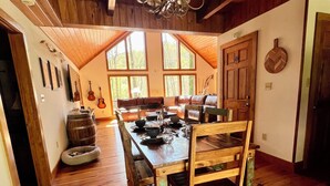 Un espace repas avec une table et des chaises en bois, un lustre et de grandes fenêtres.