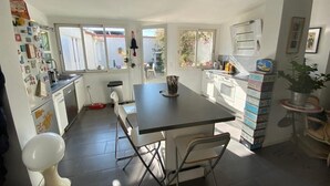 A compact kitchen with a central island, white cabinetry, and a view of the backyard through large windows. - Charming villa 2 bedrooms swimming pool Wi-Fi air conditioning parking (CANET PLAGE)