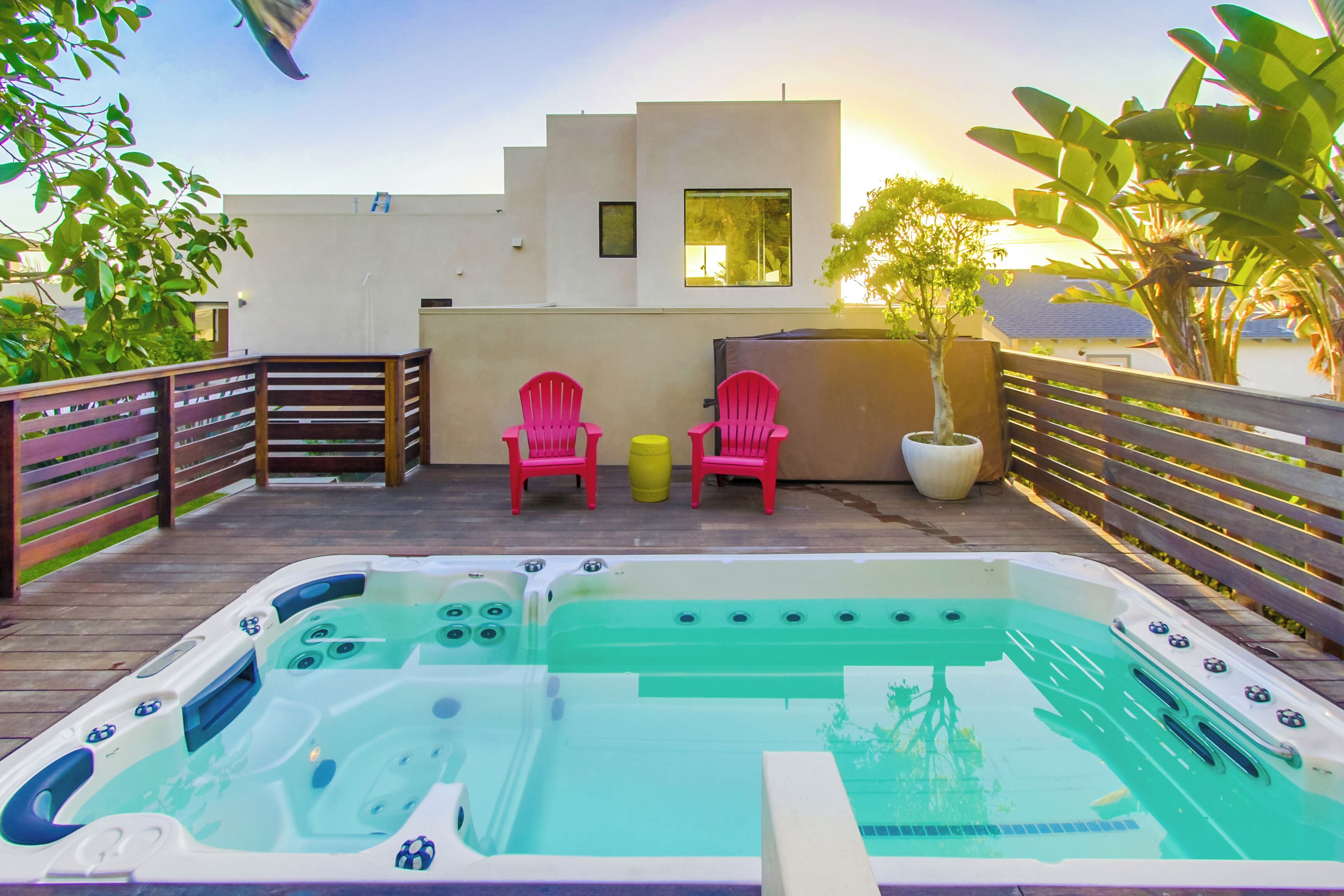 A rooftop pool area with hot tubs, two pink chairs, and potted plants.