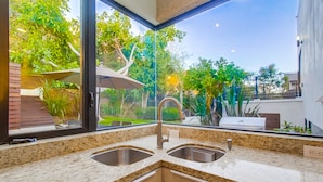 A kitchen with granite countertops, stainless steel sinks, and a window overlooking a garden.
