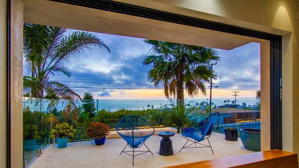 A balcony with a wooden bench, two blue chairs, a small table, and potted plants.