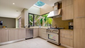 A modern kitchen with a skylight, large windows, and a view of greenery.