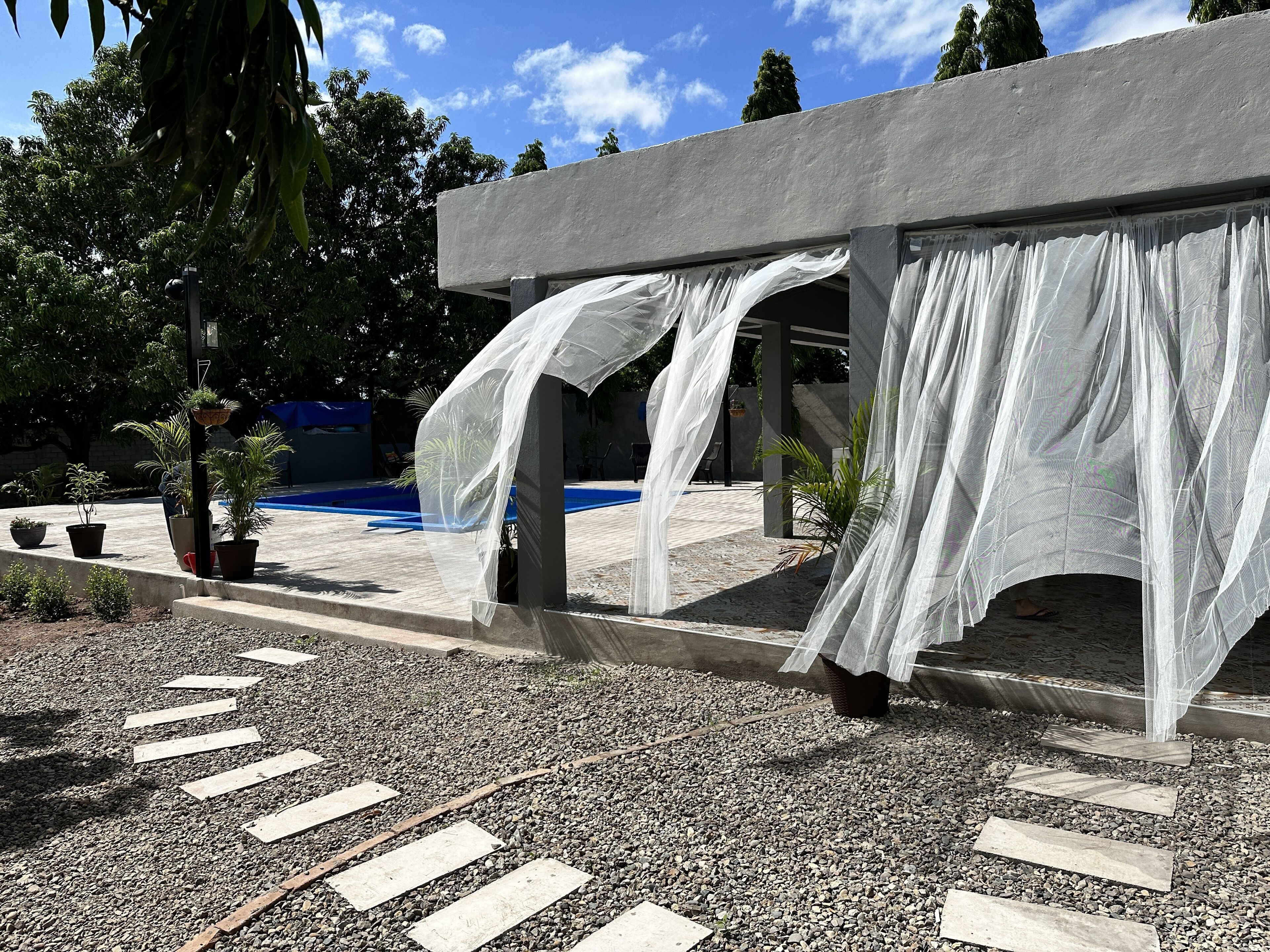 A covered outdoor area with a pool, surrounded by potted plants and a gravel path.