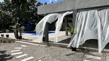 A covered outdoor area with a pool, surrounded by potted plants and a gravel path.