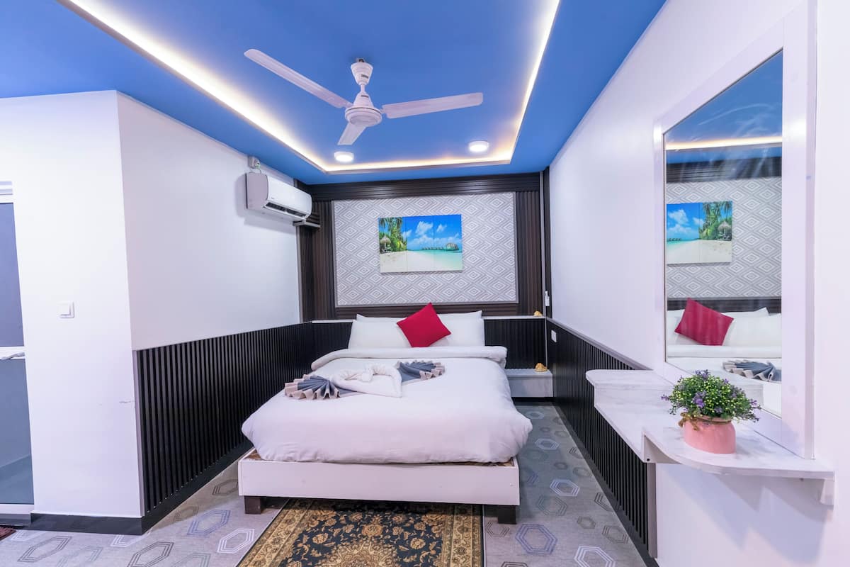 A modern bedroom with a bed, ceiling fan, air conditioning unit, and a potted plant.
