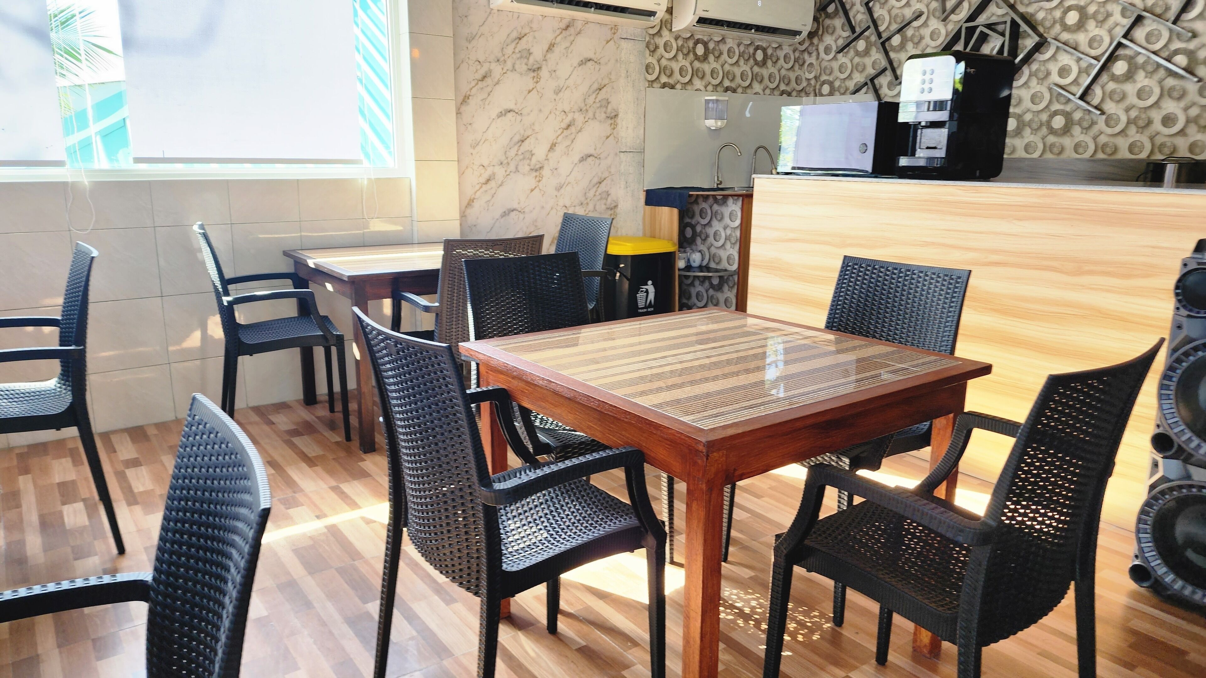 A dining area with a wooden table and black mesh chairs, a coffee machine, and a patterned wall.