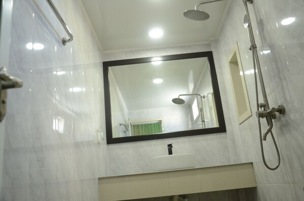 A bathroom with a large mirror, a shower, and a sink.