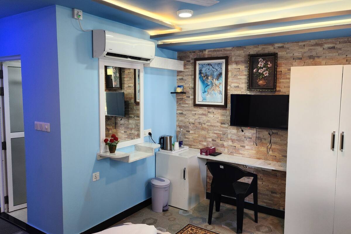 A compact room with a blue wall, a mounted air conditioner, a white cabinet, a black chair, and a TV on the wall.