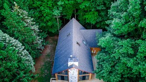An aerial view of a house with a steeply pitched roof, a deck with outdoor furniture, and a chimney.