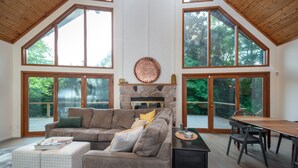 A spacious living room with a stone fireplace, large windows, and a dining area.